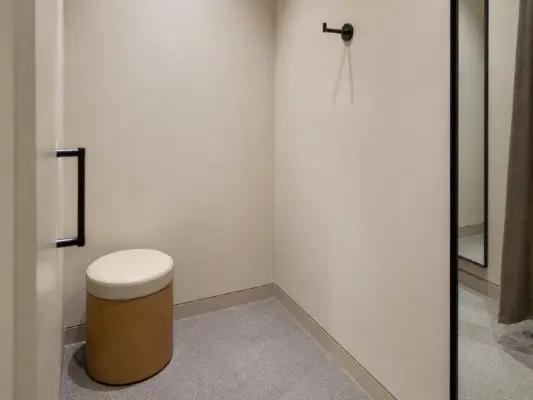 A neutral fitting room with a hook, stool and mirror